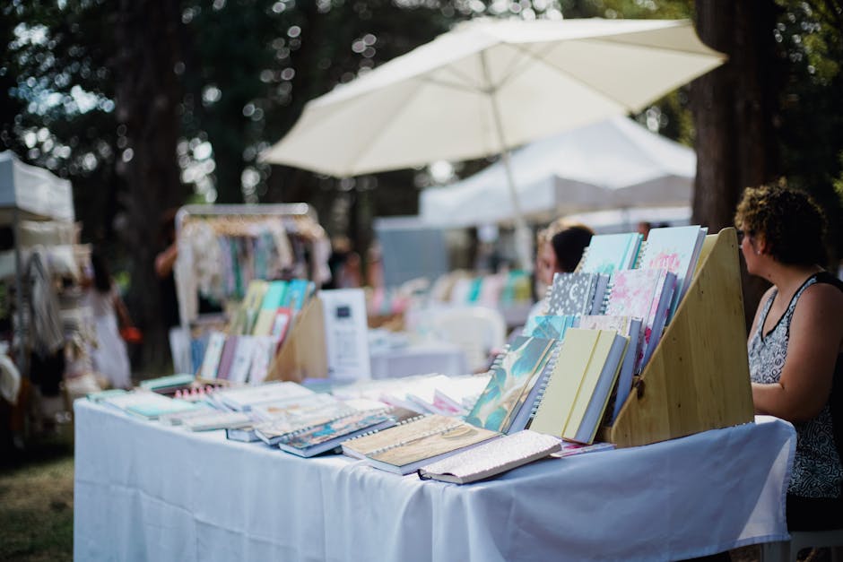 Outdoor market stall with colorful notebooks and people shopping on a sunny day.