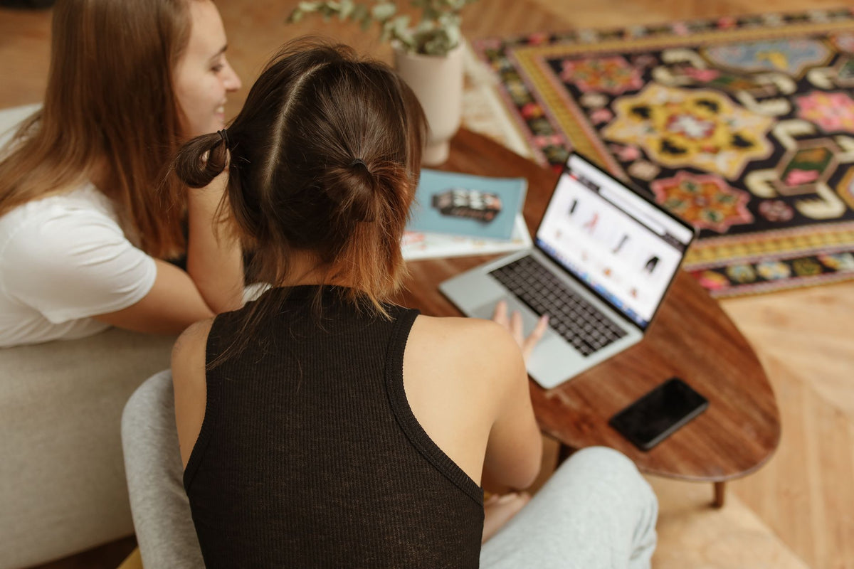 Two women engaged in online shopping sitting at home with a laptop and cozy decor.